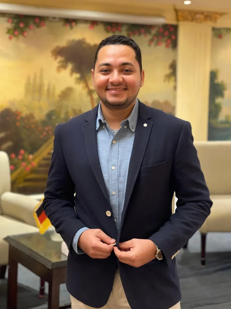 Ahmed Essam, founder of Piece of German, smiling in a navy blazer
